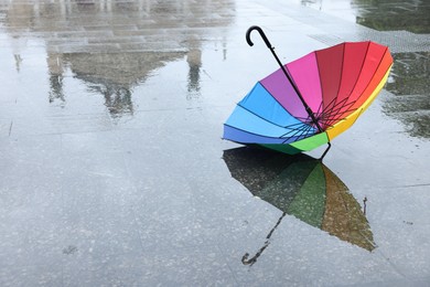 Photo of Colorful umbrella on wet asphalt outdoors, space for text
