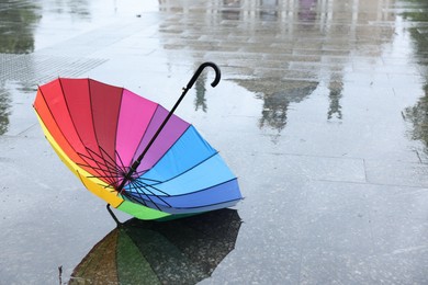 Photo of Colorful umbrella on wet asphalt outdoors, space for text