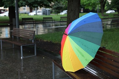 Photo of Colorful umbrella on wet bench in park, space for text