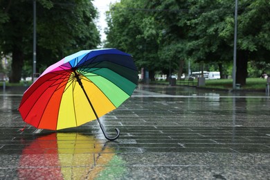Photo of Colorful umbrella on wet asphalt outdoors, space for text