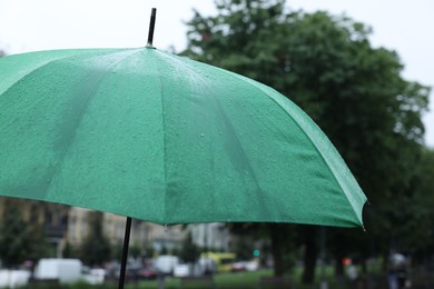 Photo of Green umbrella under heavy rain outdoors, closeup