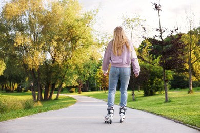 Photo of Young woman roller skating in park, back view