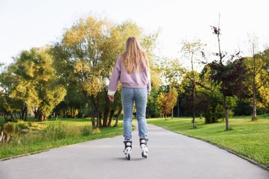 Photo of Young woman roller skating in park, back view