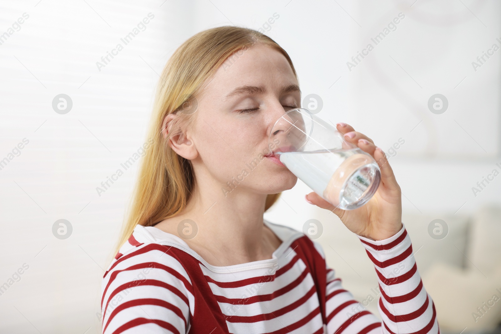 Photo of Young woman drinking water from glass at home
