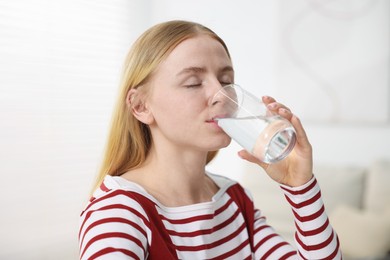 Photo of Young woman drinking water from glass at home