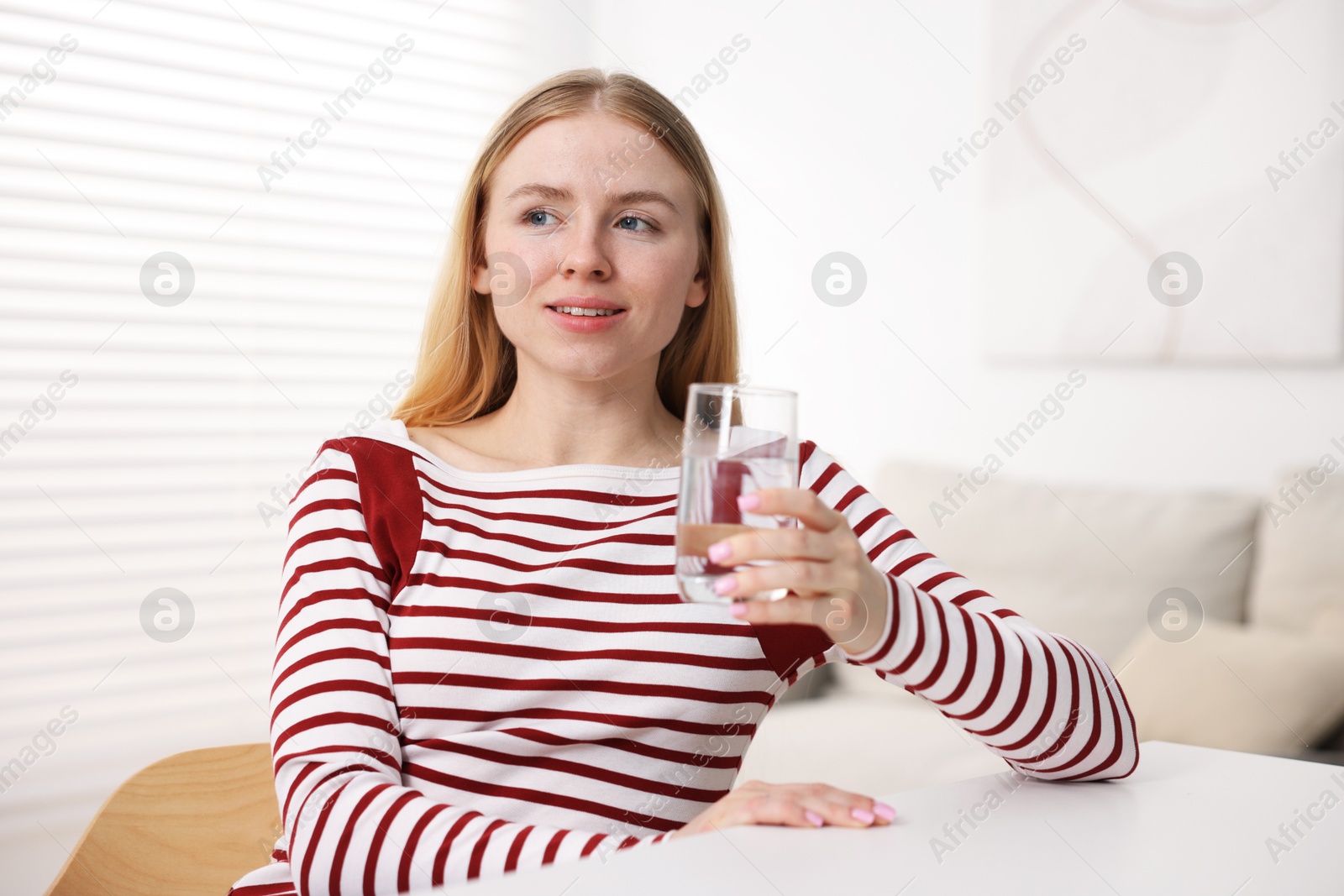 Photo of Young woman with glass of water at white table indoors