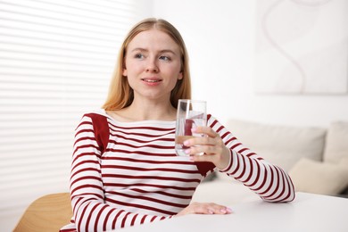 Photo of Young woman with glass of water at white table indoors