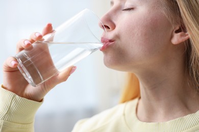 Photo of Young woman drinking water from glass at home, closeup