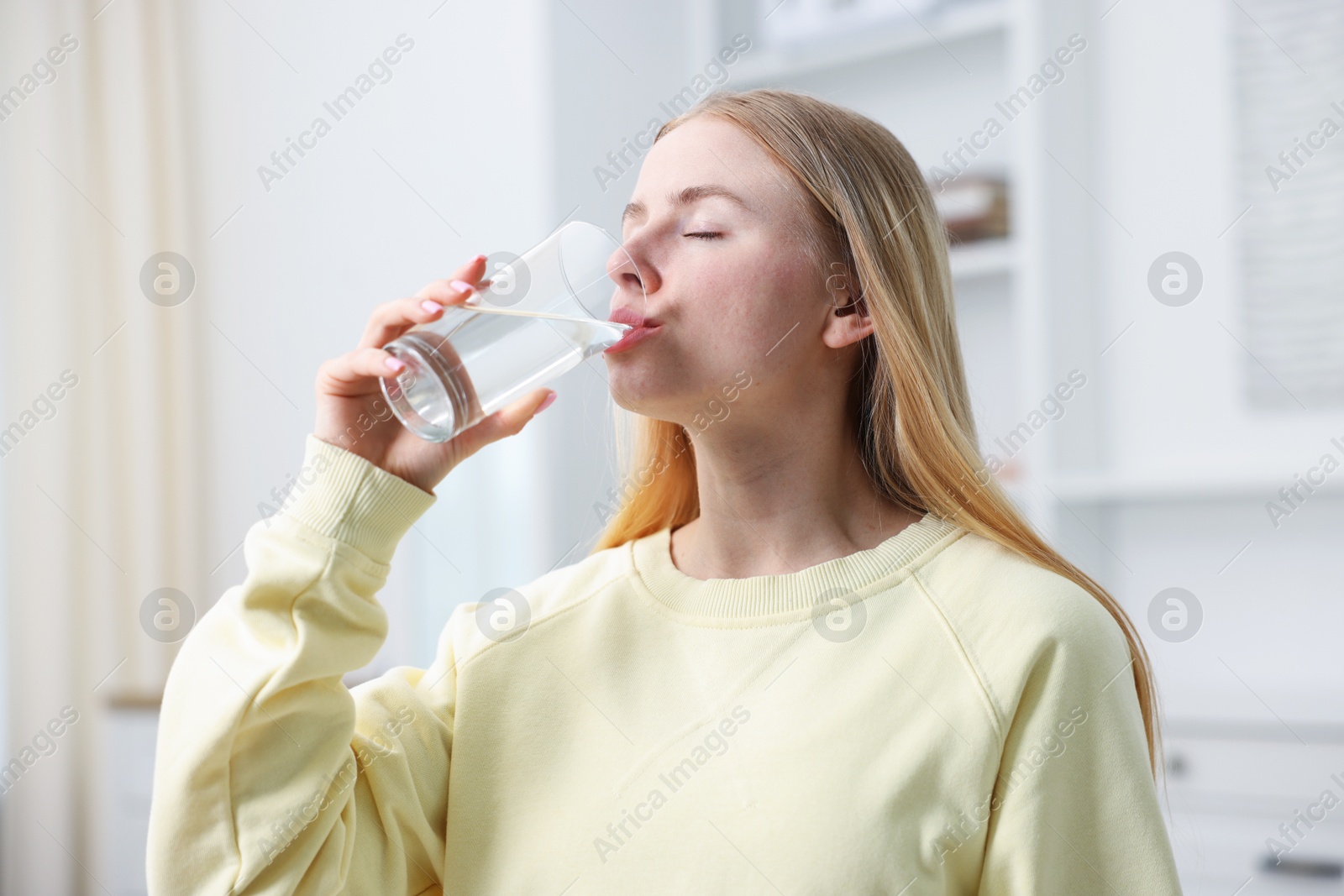 Photo of Young woman drinking water from glass at home
