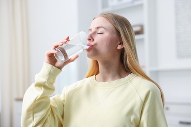 Photo of Young woman drinking water from glass at home