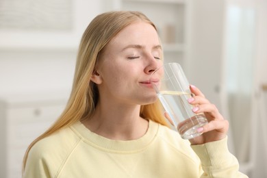 Photo of Young woman drinking water from glass at home