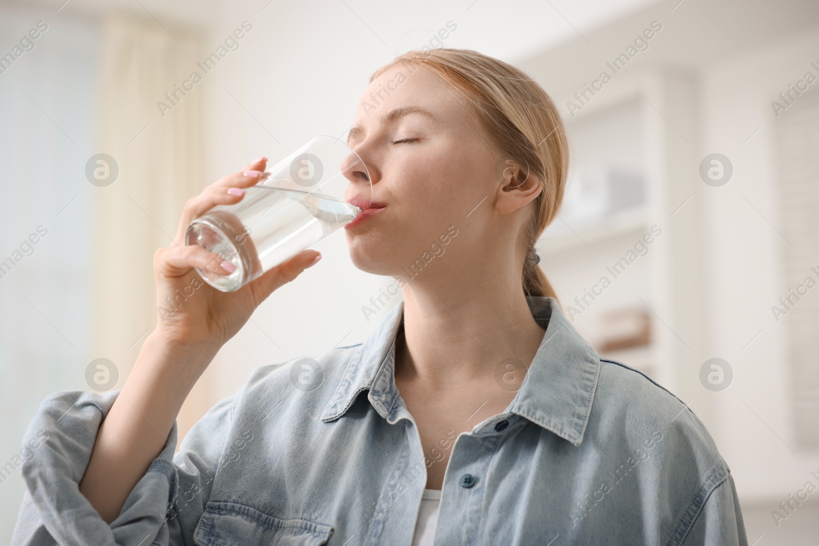 Photo of Young woman drinking water from glass at home