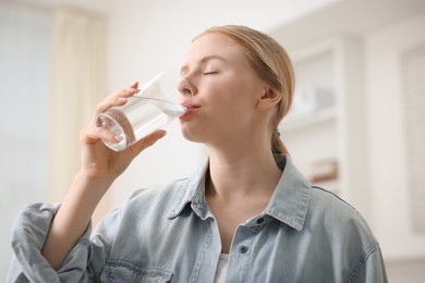 Photo of Young woman drinking water from glass at home