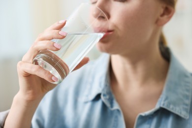 Photo of Young woman drinking water from glass at home, closeup