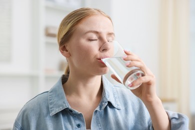 Photo of Young woman drinking water from glass at home