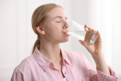 Photo of Young woman drinking water from glass at home