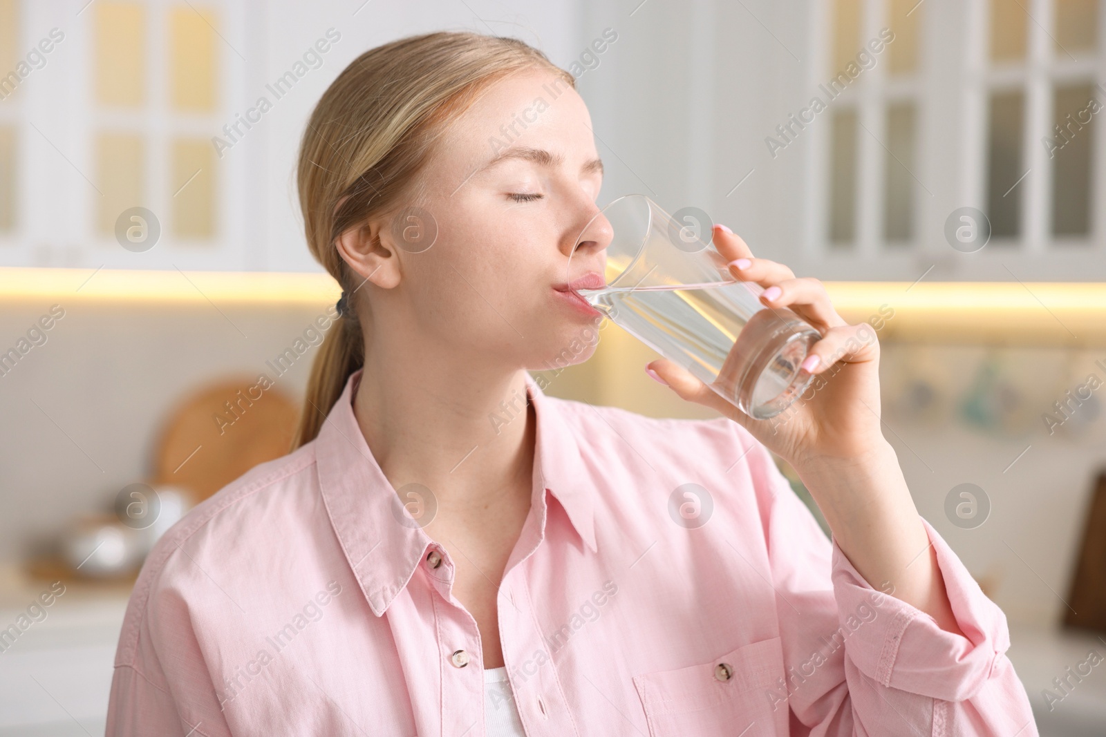Photo of Young woman drinking water from glass in kitchen