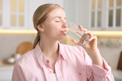 Photo of Young woman drinking water from glass in kitchen