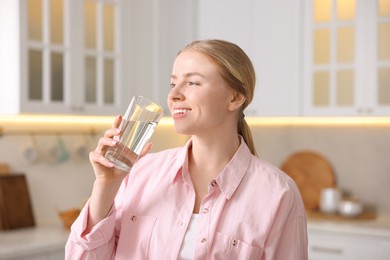 Photo of Young woman drinking water from glass in kitchen