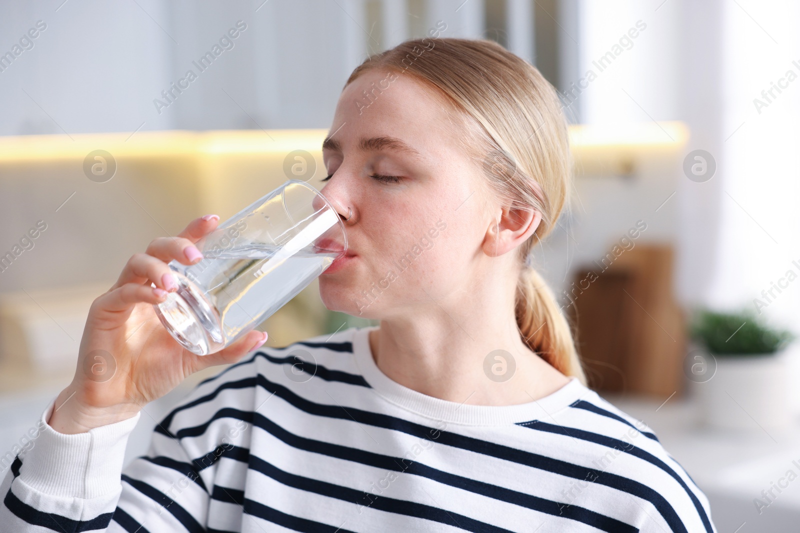 Photo of Young woman drinking water from glass in kitchen