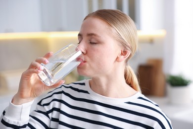 Photo of Young woman drinking water from glass in kitchen