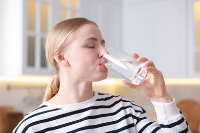 Photo of Young woman drinking water from glass in kitchen