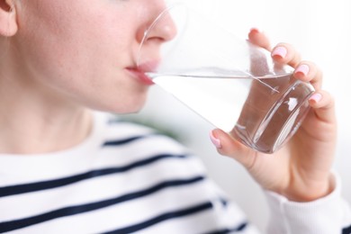 Photo of Young woman drinking water from glass at home, closeup