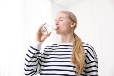 Photo of Young woman drinking water from glass on light background, low angle view