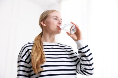 Photo of Young woman drinking water from glass on light background, low angle view
