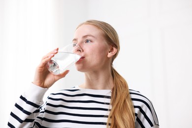Photo of Young woman drinking water from glass on light background, low angle view