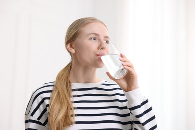 Photo of Young woman drinking water from glass on light background, low angle view