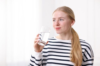 Photo of Young woman drinking water from glass on light background