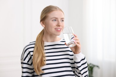 Photo of Young woman drinking water from glass at home