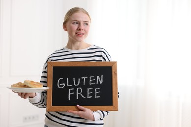 Photo of Woman holding small chalkboard with text Gluten Free and pretzels indoors. Space for text