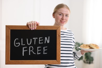 Photo of Woman holding small chalkboard with text Gluten Free and pretzels indoors, selective focus