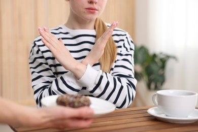 Photo of Gluten free diet. Woman refusing from donut at wooden table indoors, closeup