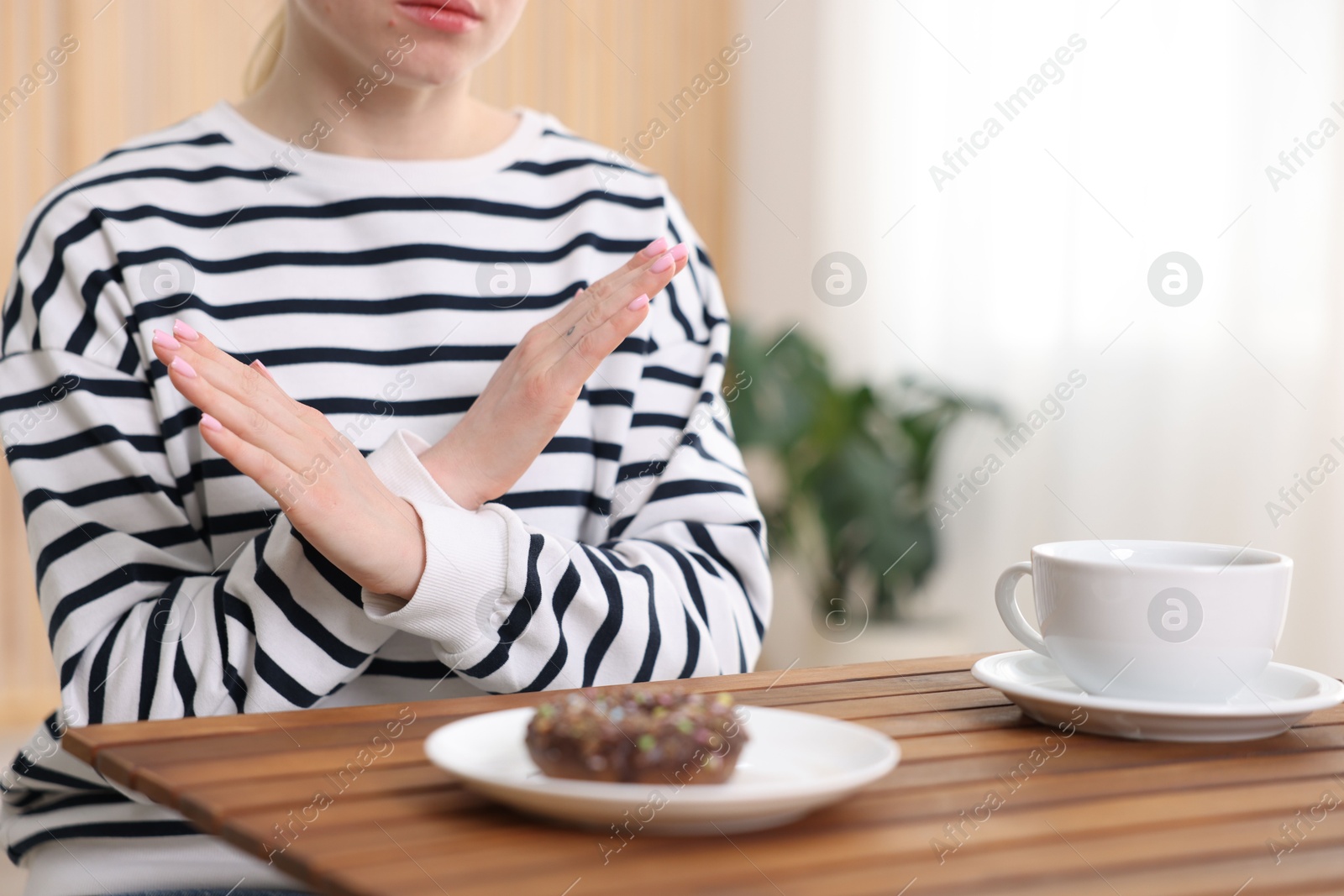 Gluten free diet. Woman refusing from donut at wooden table indoors, closeup Photo of Gluten free diet. Woman refusing from donut at wooden table indoors, closeup