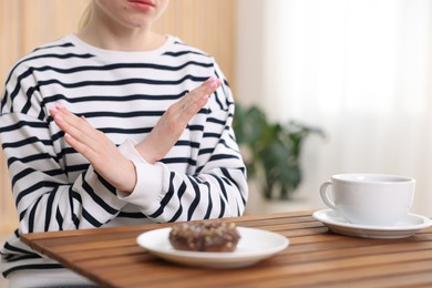 Photo of Gluten free diet. Woman refusing from donut at wooden table indoors, closeup