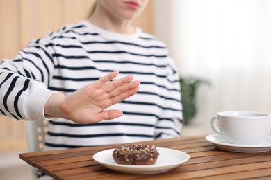 Photo of Gluten free diet. Woman refusing from donut at wooden table indoors, closeup