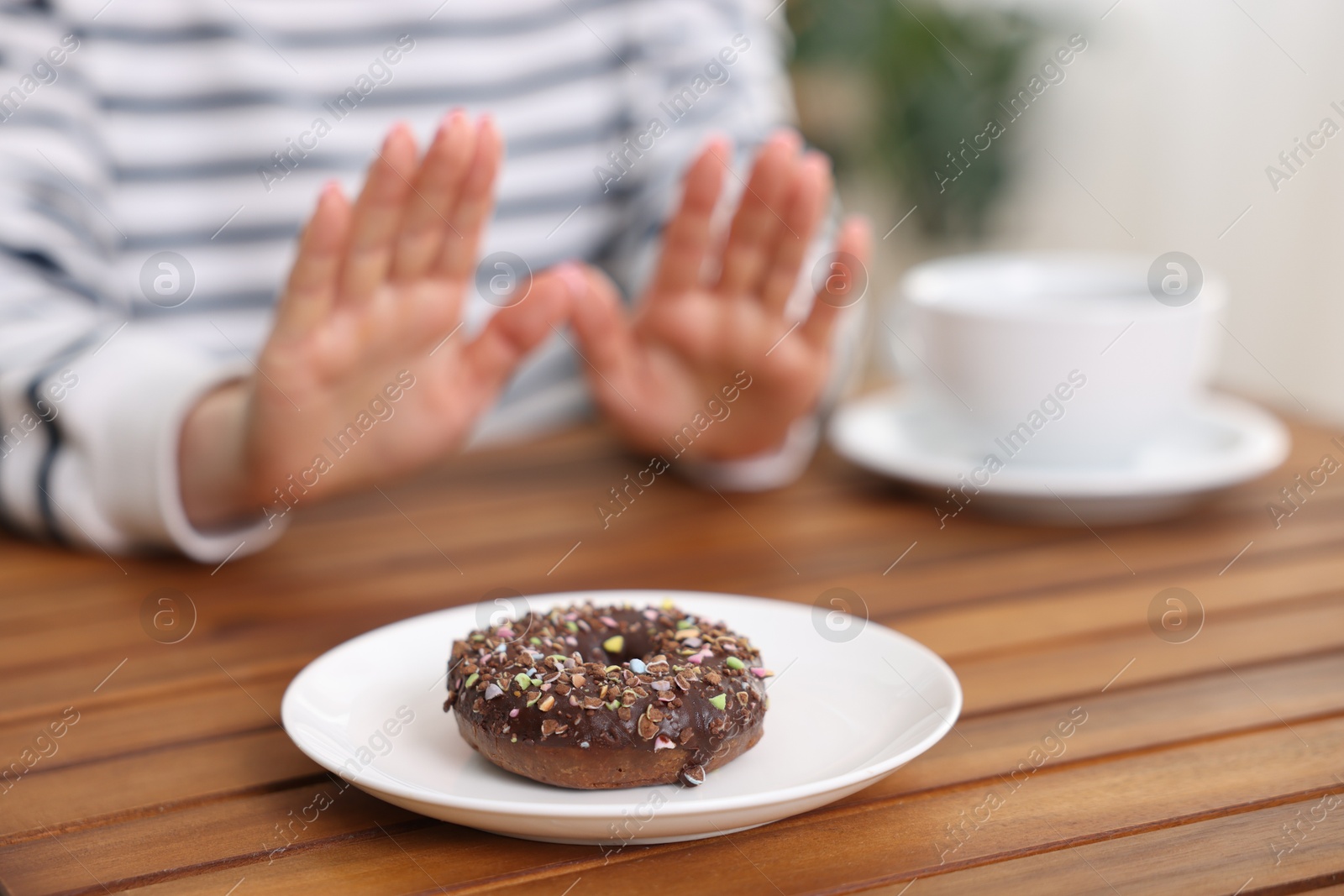 Gluten free diet. Woman refusing from donut at wooden table indoors, selective focus Photo of Gluten free diet. Woman refusing from donut at wooden table indoors, selective focus