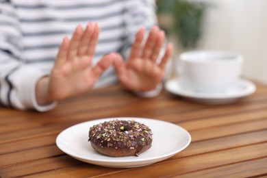 Photo of Gluten free diet. Woman refusing from donut at wooden table indoors, selective focus