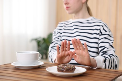 Photo of Gluten free diet. Woman refusing from donut at wooden table indoors, closeup