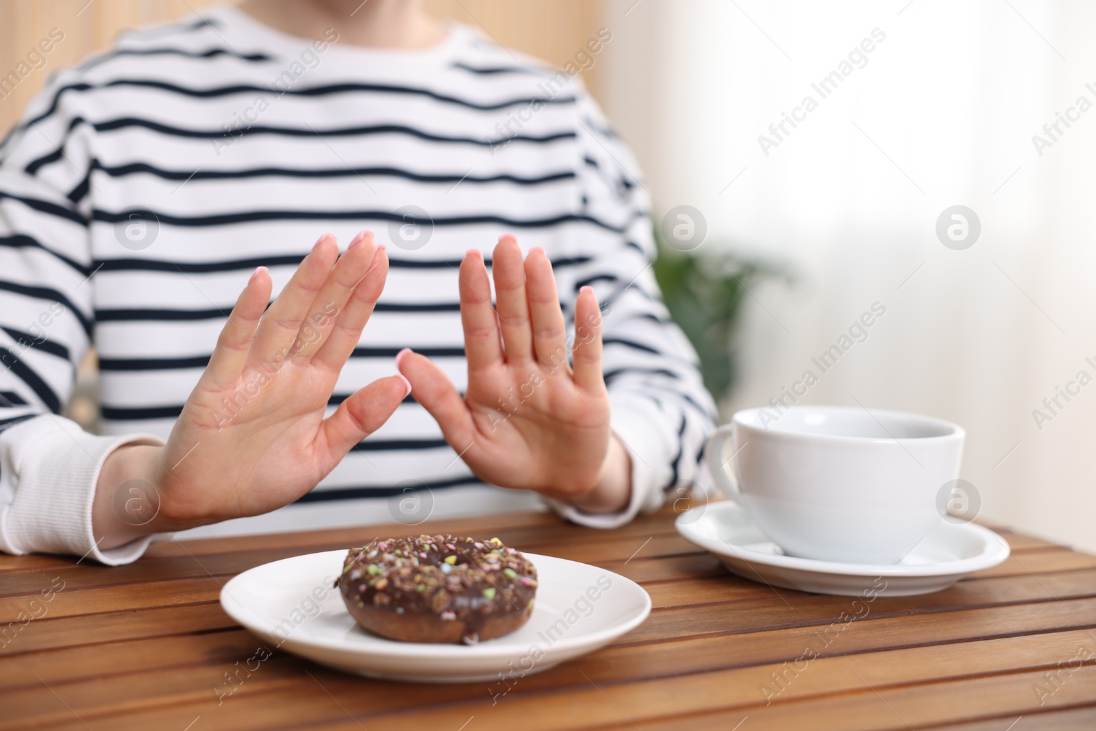 Gluten free diet. Woman refusing from donut at wooden table indoors, closeup Photo of Gluten free diet. Woman refusing from donut at wooden table indoors, closeup