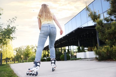 Photo of Young woman roller skating outdoors, back view