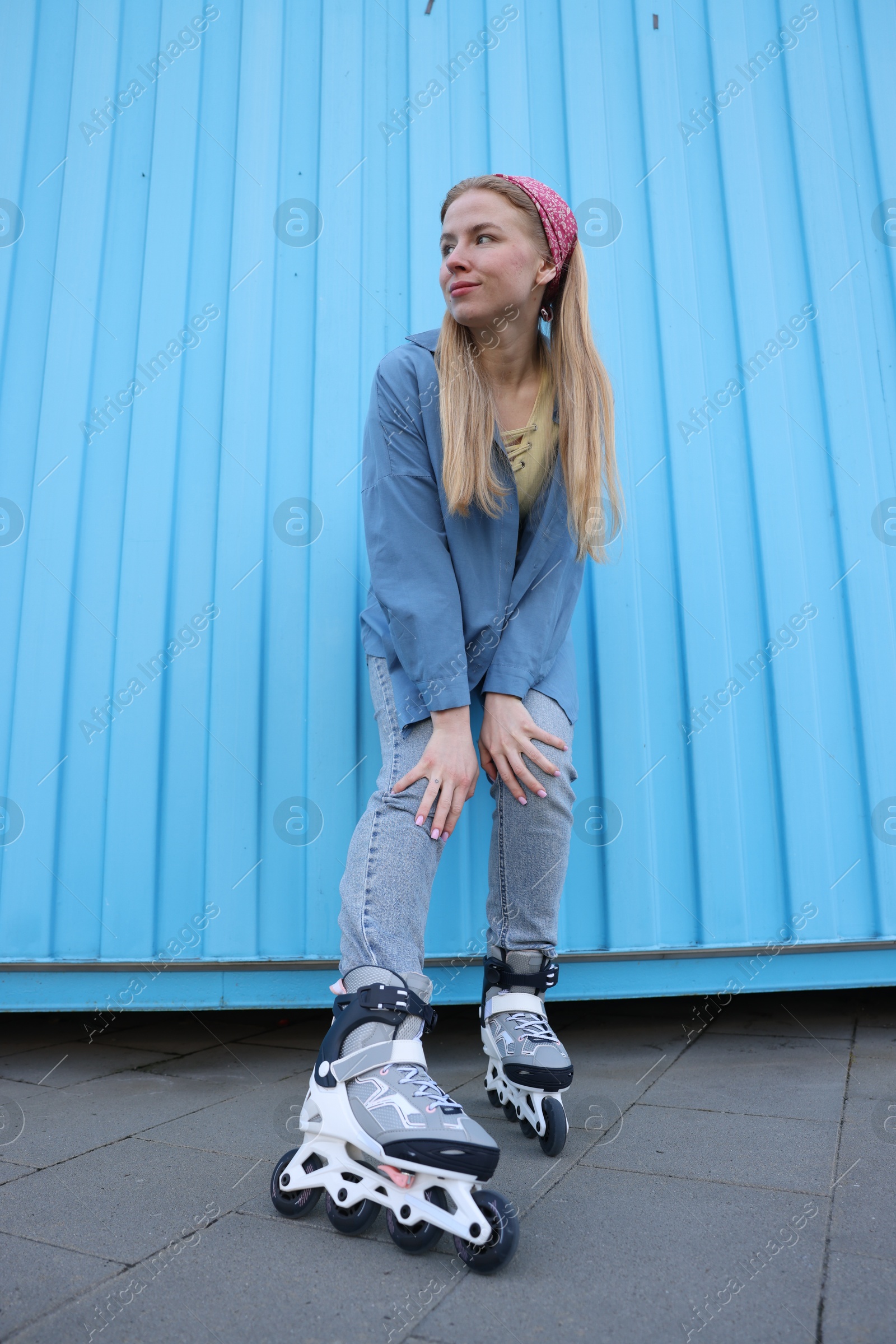 Beautiful young woman with roller skates near light blue wall outdoors, low angle view Photo of Beautiful young woman with roller skates near light blue wall outdoors, low angle view
