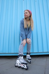 Photo of Beautiful young woman with roller skates near light blue wall outdoors, low angle view