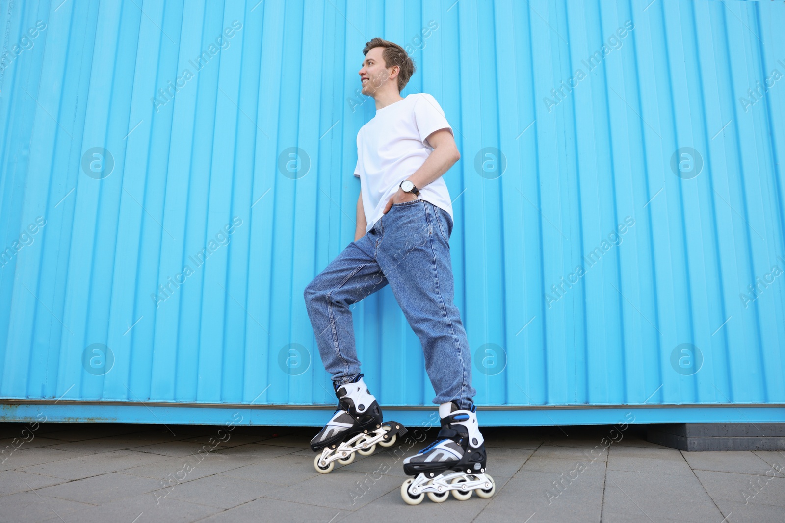 Happy young man with roller skates near light blue wall outdoors, low angle view Photo of Happy young man with roller skates near light blue wall outdoors, low angle view