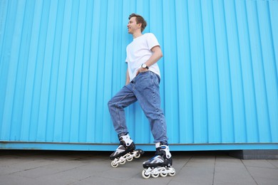 Photo of Happy young man with roller skates near light blue wall outdoors, low angle view