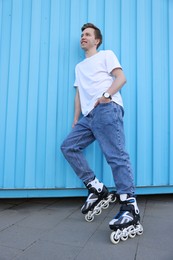 Photo of Happy young man with roller skates near light blue wall outdoors, low angle view