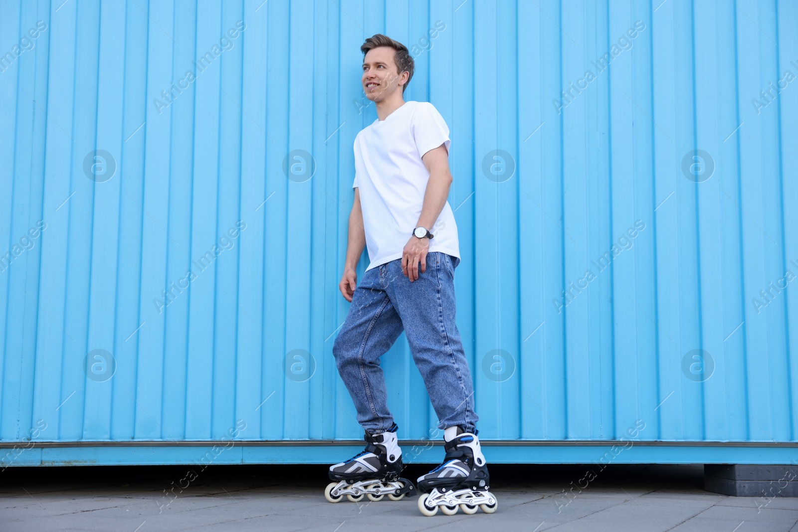 Photo of Happy young man with roller skates near light blue wall outdoors